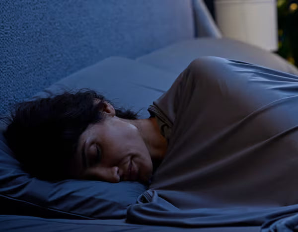 Model sleeping under Original Performance Sheet Sets in Graphite in a dimly lit room