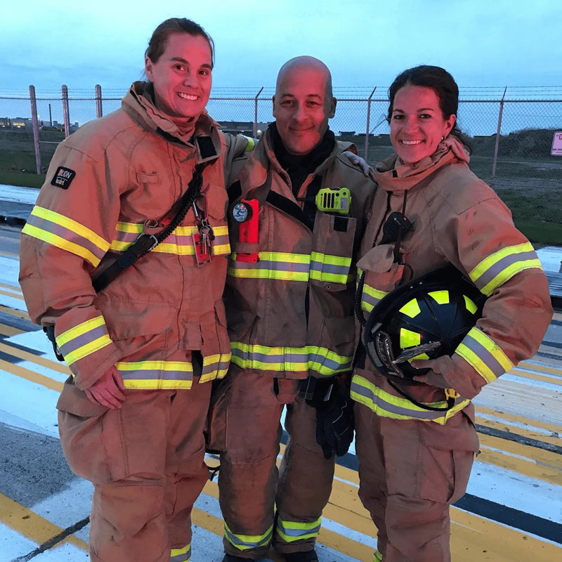 Three firefighters posing together outdoors with a clear sky background