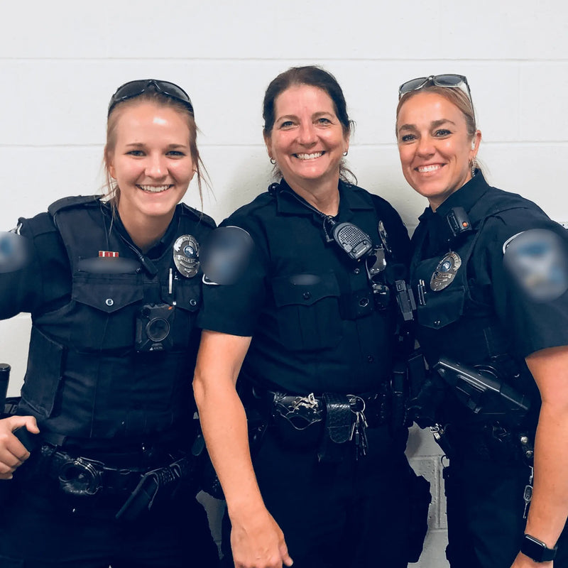 Three police officers posing together against a white wall.