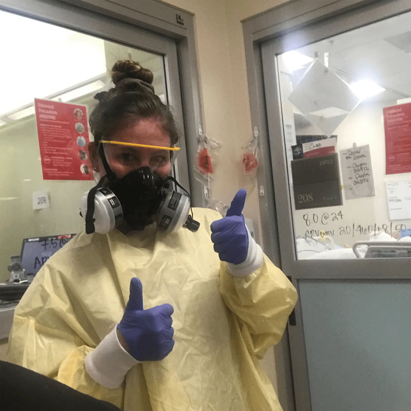 Person in protective gear giving a thumbs-up gesture in a clinical setting.