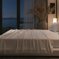 Modern bedroom with a large bed, nightstands, and a lamp near a window with curtains. Bed has Nightfall Sheet Sets in Cloud White color.#choose-your-color_cloud-white