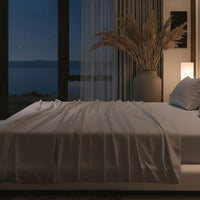 Modern bedroom with a large bed, nightstands, and a lamp near a window with curtains. Bed has Nightfall Sheet Sets in Silver Dusk color.#choose-your-color_silver-dusk
