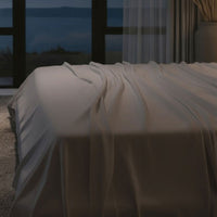 Modern bedroom with a large bed, nightstands, and a lamp near a window with curtains. Bed has Nightfall Sheet Sets in Silver Dusk color.#choose-your-color_silver-dusk