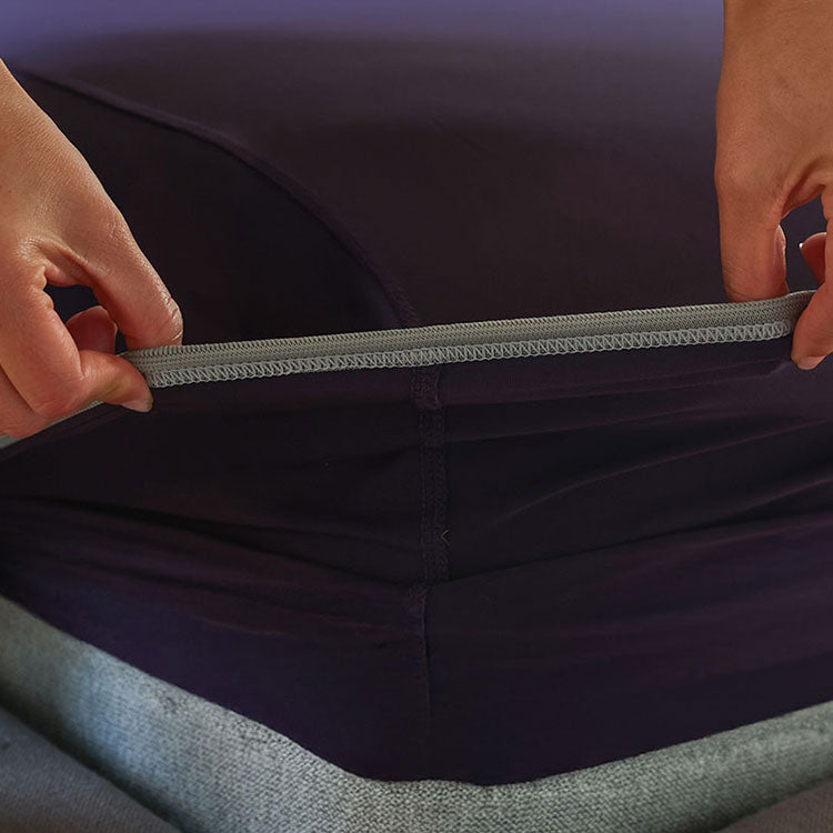Royal Plum fitted sheet being stretched over a bed showing deep pocket. #choose-your-color_royal-plum