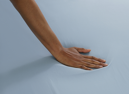 A close-up of a person's hand pressing into a smooth, light blue fabric surface, demonstrating its soft texture and elasticity.