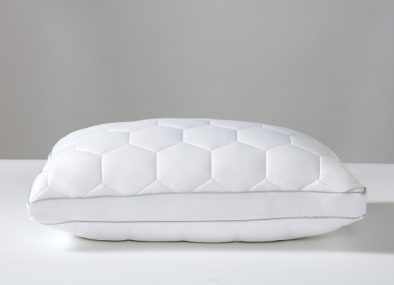 A white quilted pillow with a hexagonal stitched pattern, resting on a white surface against a neutral gray background.