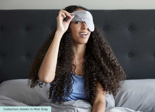 midnight label-sleep mask + travel pouch - mist gray color on model in bed with one eye winking #choose-your-color_porcelain