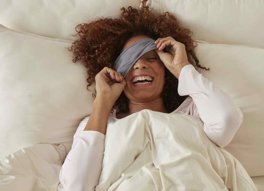 SHEEX Sleep Mask in Graphite on model in bed covering one eye with smile